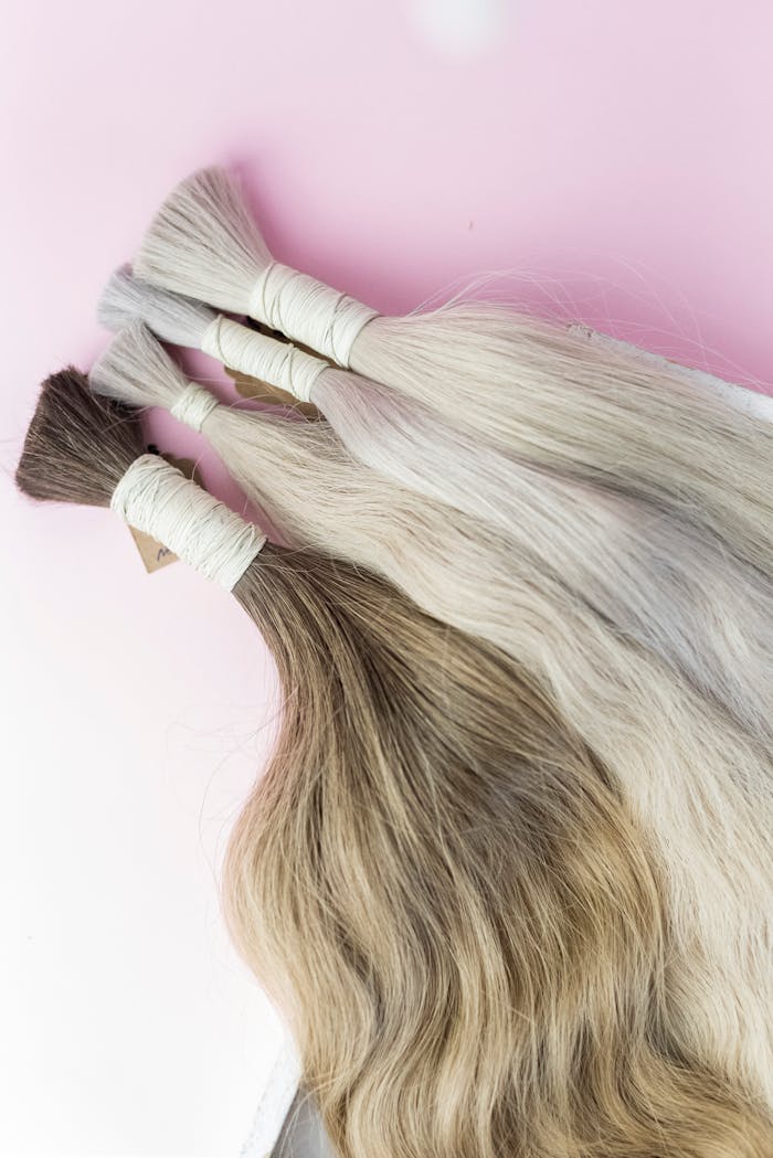 Close-up view of diverse human hair extensions on a soft pink surface.