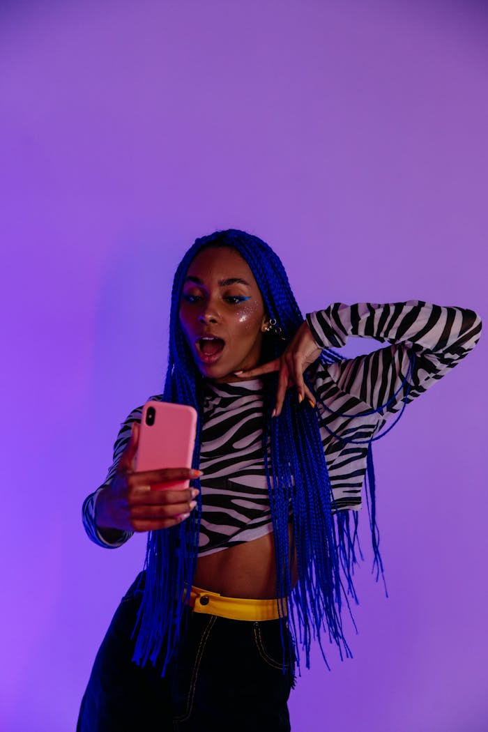 Fashionable woman with blue hair posing for a selfie against a purple background.